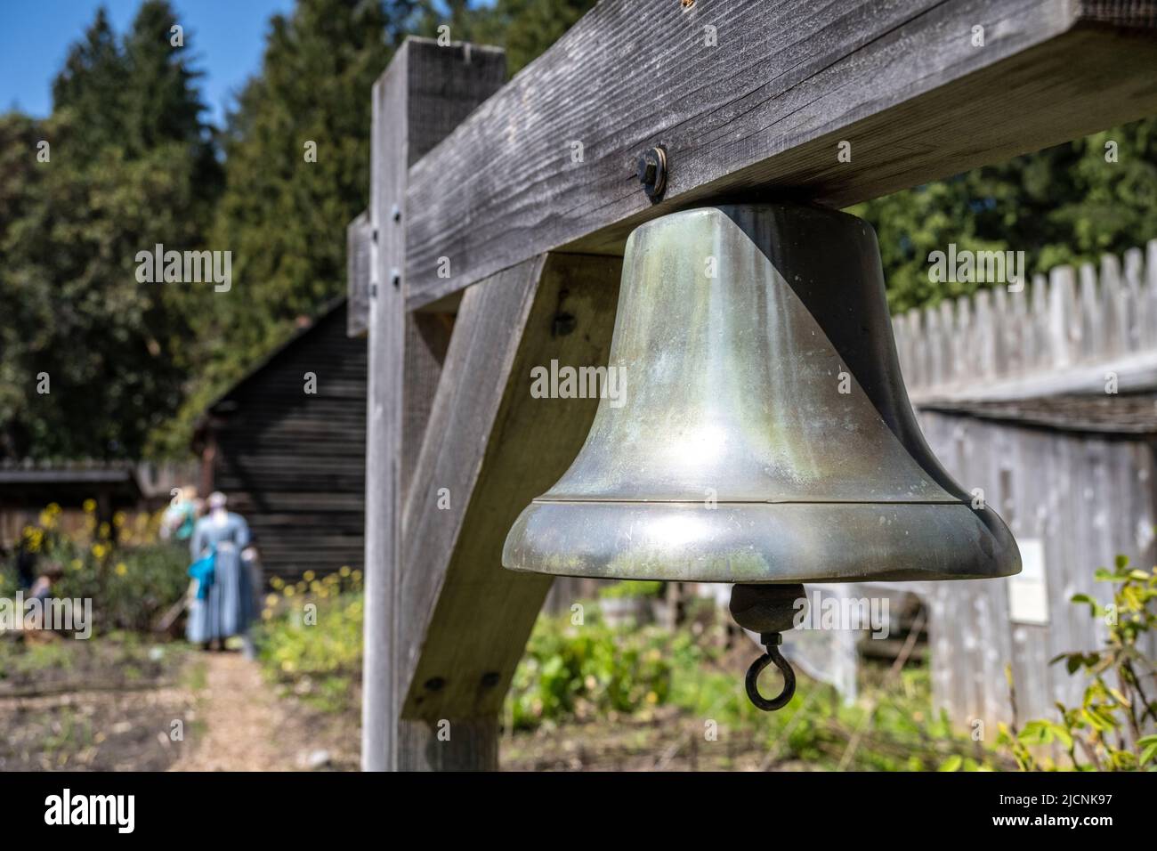 bell on lthe grounds of Fort Nisqually Living History Museum with women in traditional clothing worn in the 1850s Stock Photo