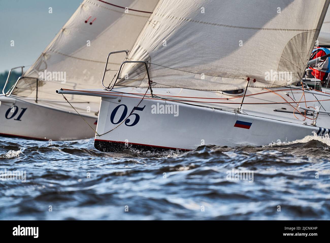 Bowsprits of sailing yachts in sailing regatta at sunset, still water, the clear sky, hot racing