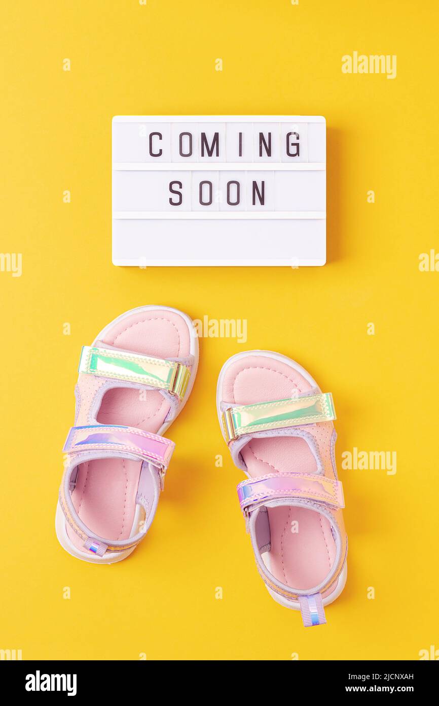 Coming soon. Motivational quote on lightbox and stylish holographic sandals on yellow background. Top view, Flat lay. Creative inspirational concept. Stock Photo