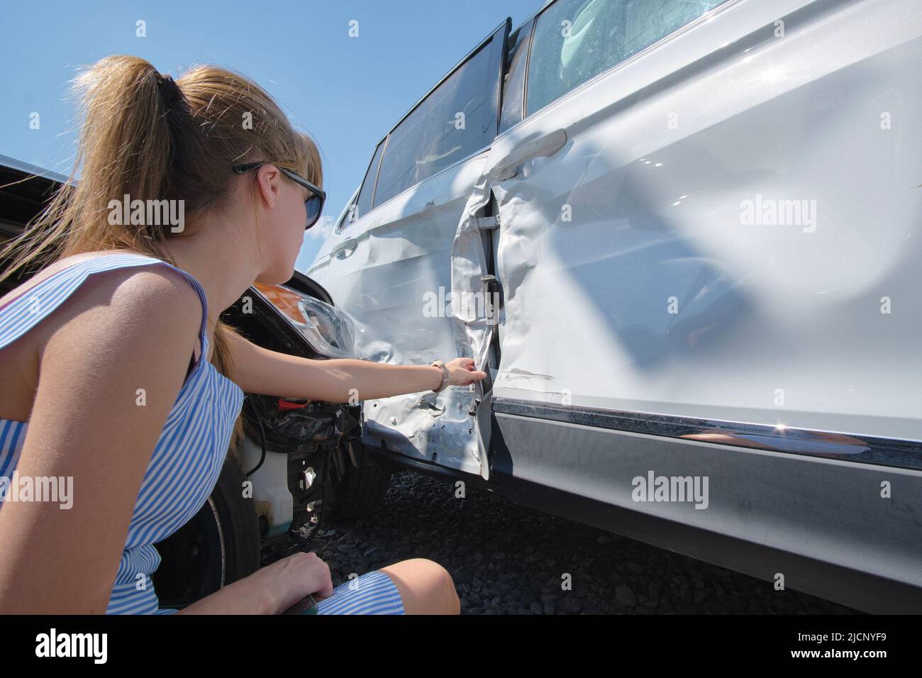 Sad female driver sitting on street side shocked after car accident. Road safety and vehicle insurance concept Stock Photo