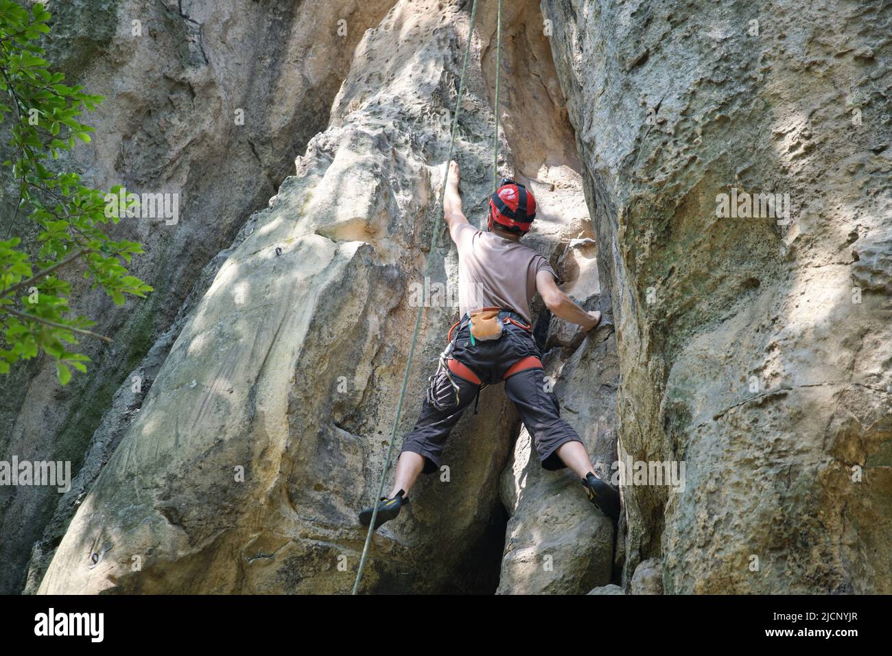 Strong male climber climbing steep wall of rocky mountain. Sportsman difficult route