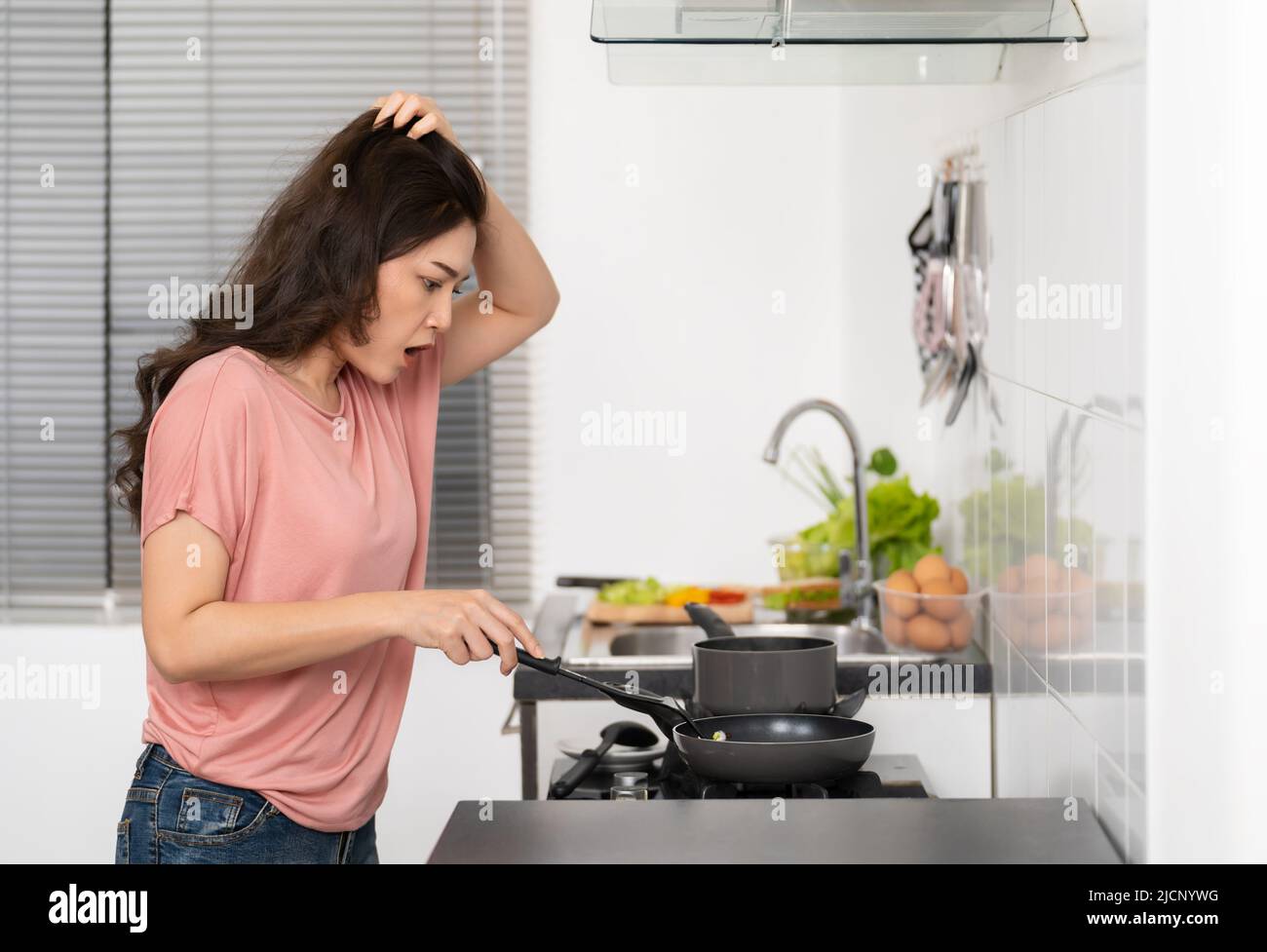 stressed young woman cooking and preparing food in the kitchen at home Stock Photo