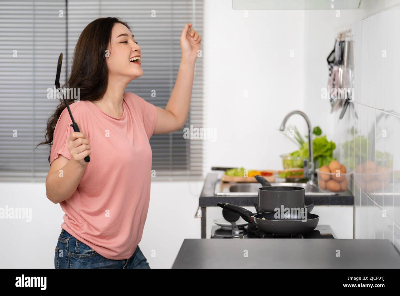cheerful young woman dancing while cooking food in the kitchen at home