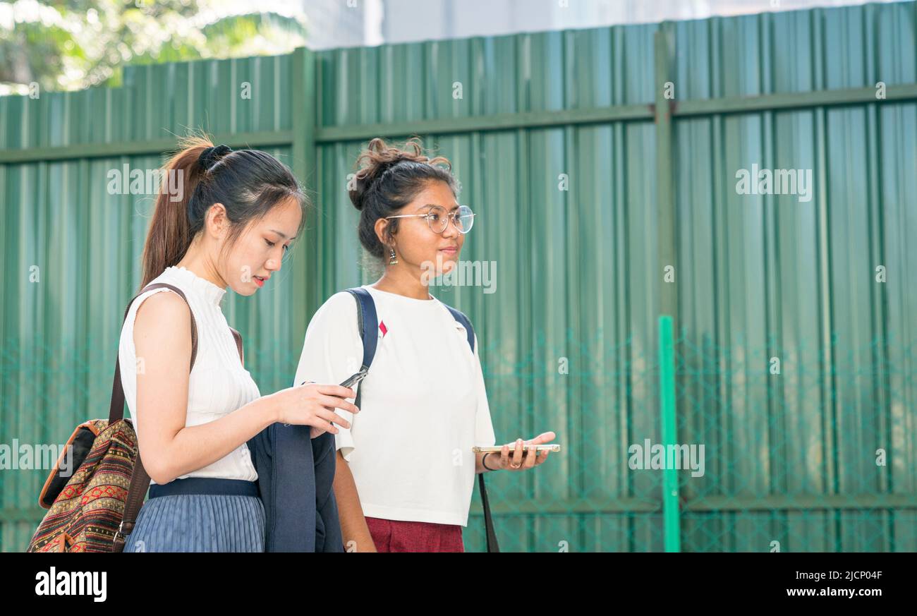 Two young women multi-racial with their mobile phones while walking together. Stock Photo