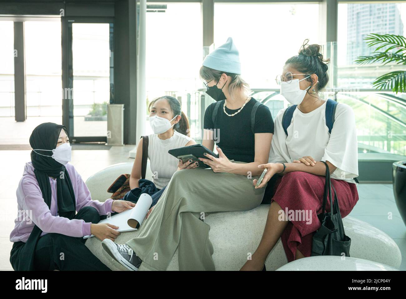 Group of multi-racial young women wearing face mask sitting and hanging out together. Stock Photo