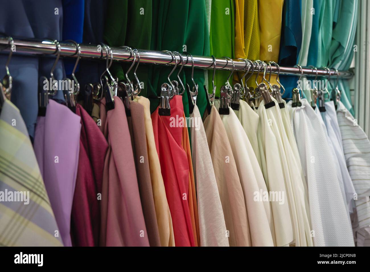 Samples of bright color fabrics hang on metal rack bar Stock Photo