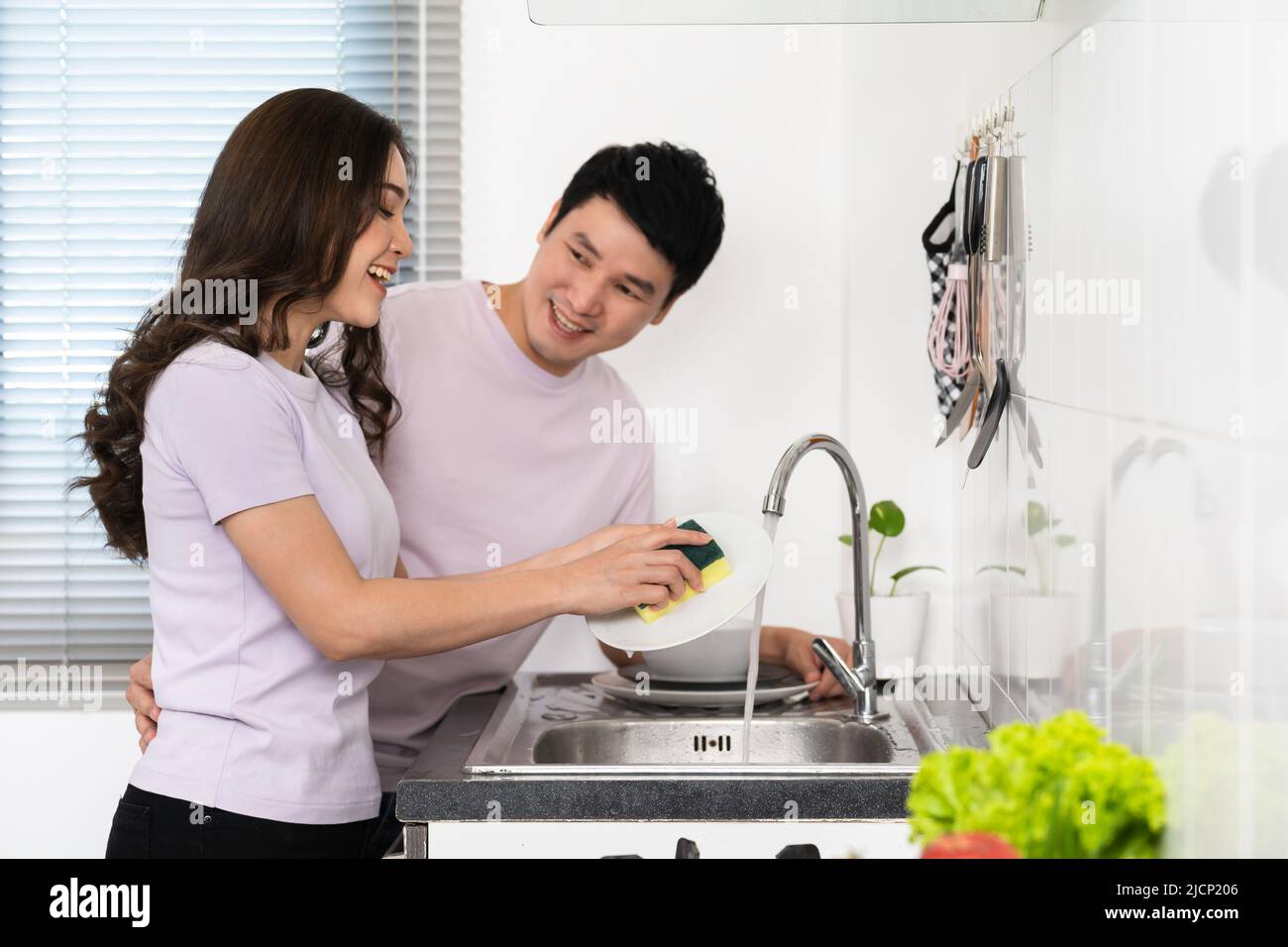 happy young couple washing dishes together in the sink in the kitchen at home Stock Photo