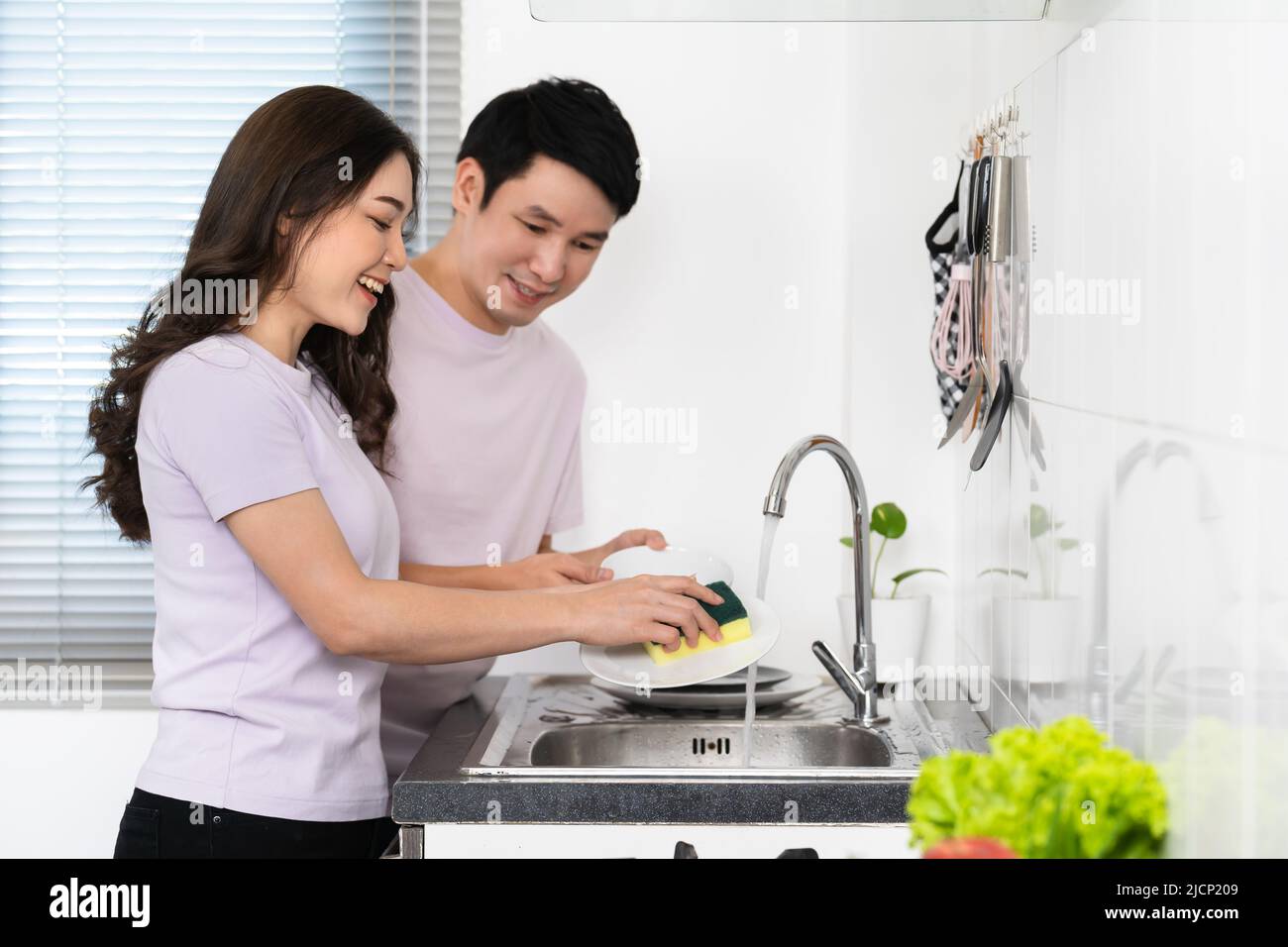 happy young couple washing dishes together in the sink in the kitchen at home Stock Photo
