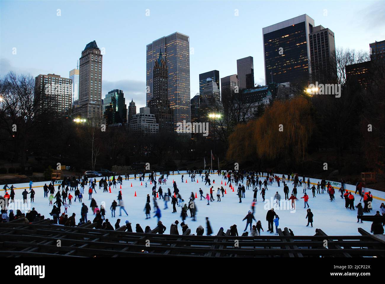 A crowd of ice skaters enjoy winter recreation skating around Wollman Rink in Central Park with the New York City and Manhattan skyline behind them Stock Photo