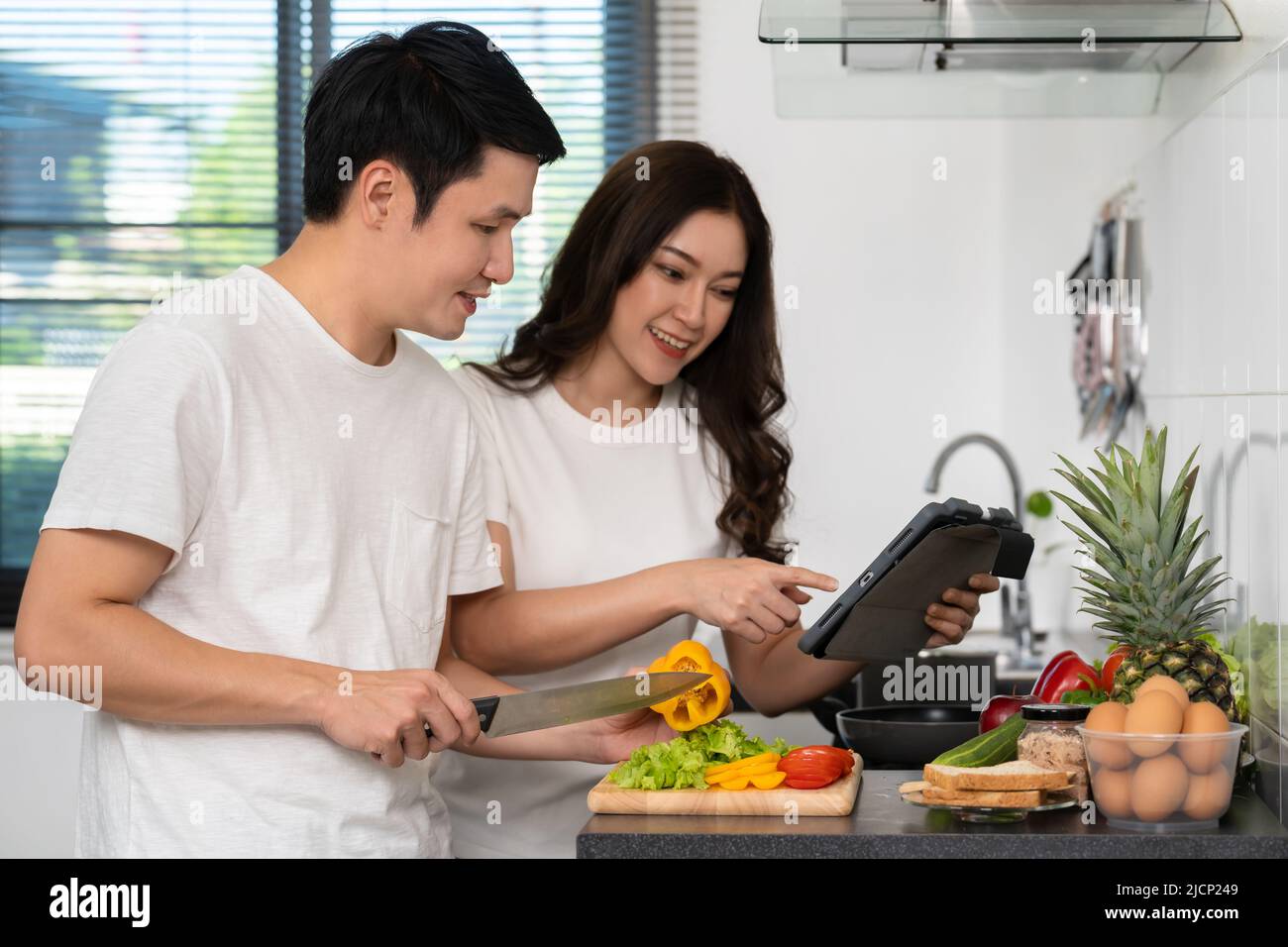 couple cooking and preparing vegetables according to a recipe on a tablet computer in the kitchen at home Stock Photo