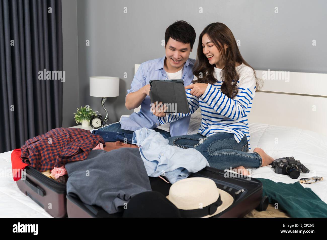 couple writing tablet and packing clothes into suitcase on a bed at home, planning travel holiday. Stock Photo