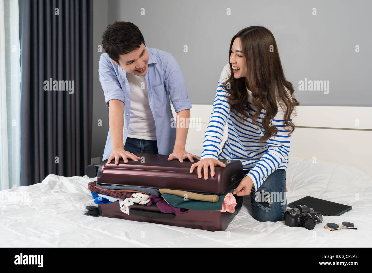 cheerful couple trying to close suitcase on a bed at home, holiday travel concept Stock Photo