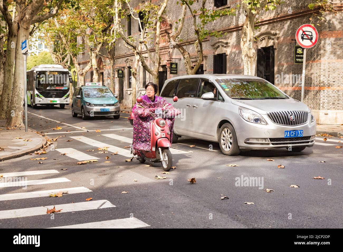 30 November 2018: Shanghai, China - Woman riding electric scooter with body blanket attachment to keep warm. Stock Photo