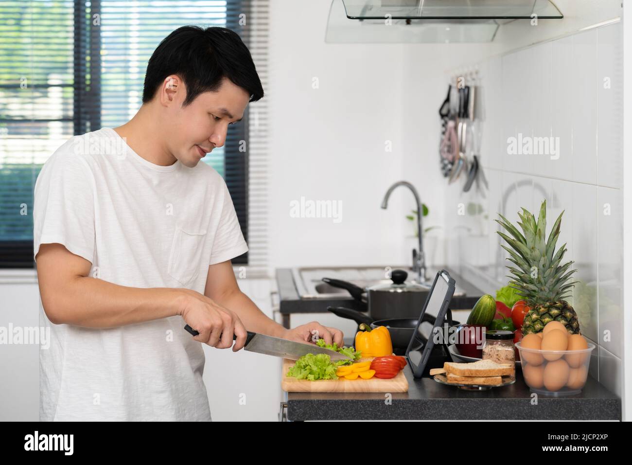man cooking and preparing vegetables according to a recipe on a tablet computer in the kitchen at home Stock Photo