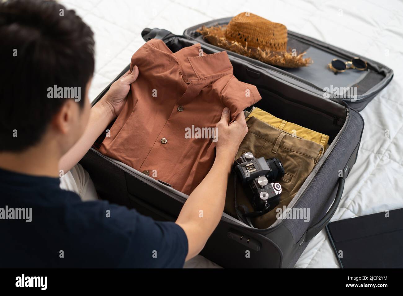 young man preparing and packing clothes into suitcase on bed at home, holiday travel concept Stock Photo