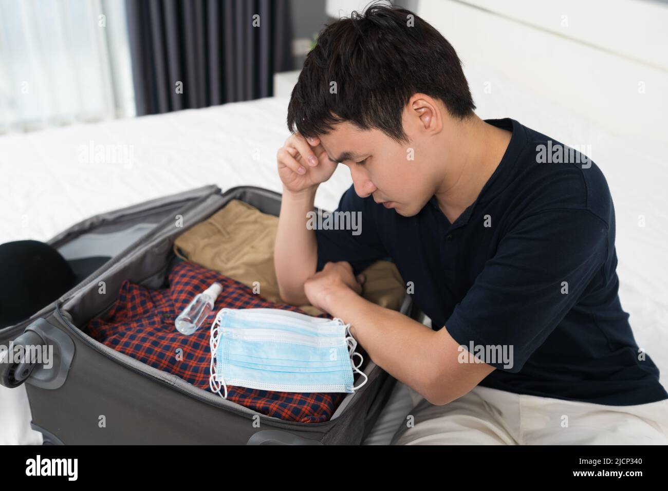 stress man packing suitcase luggage including face mask and alcohol spray to protect coronavirus (covid-19) on a bed Stock Photo
