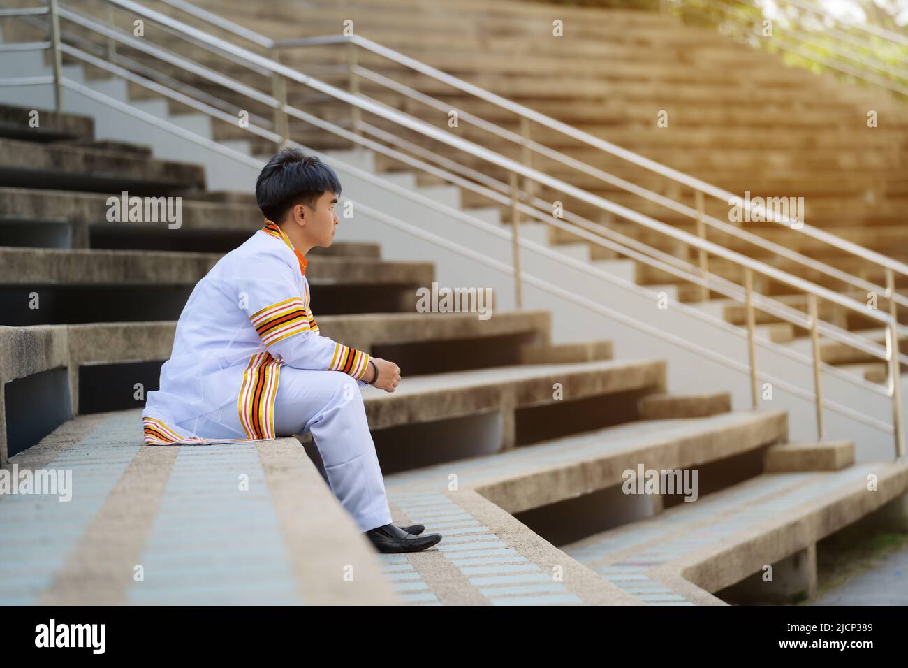 young man university graduates in graduation gown sitting on stairs Stock Photo