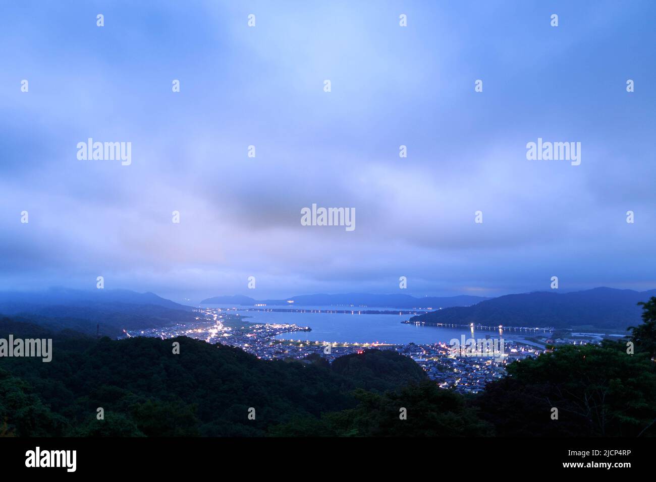 Last glow of sunset hits clouds over small city on coast at blue hour Stock Photo