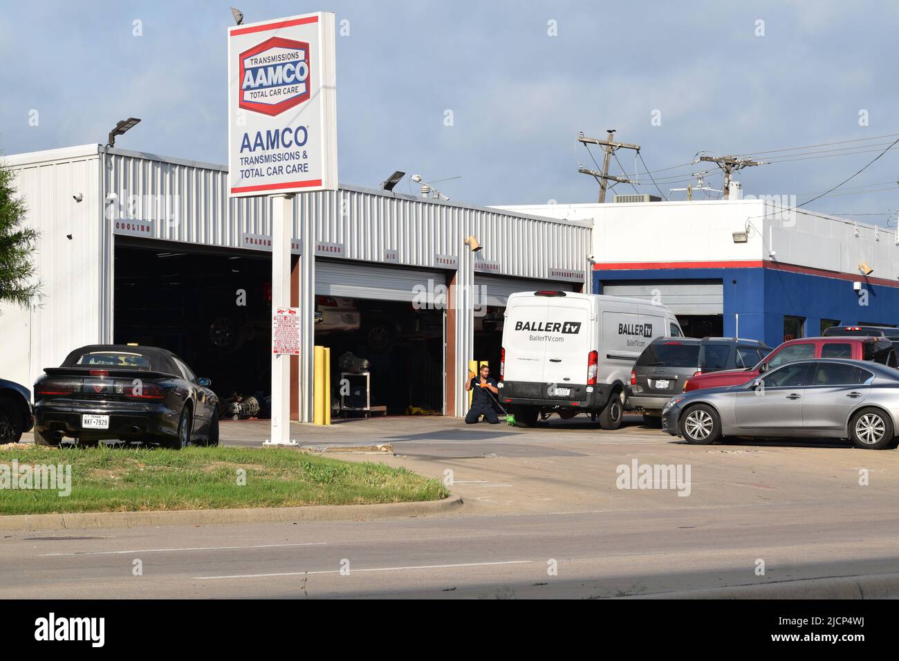 A mechanic using a jack to lift a work van outside an Aamco Transmissions and Total Car Care shop Stock Photo