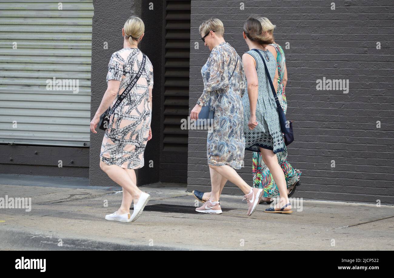 Four women walking down a city side walk, three women wearing long dresses Stock Photo