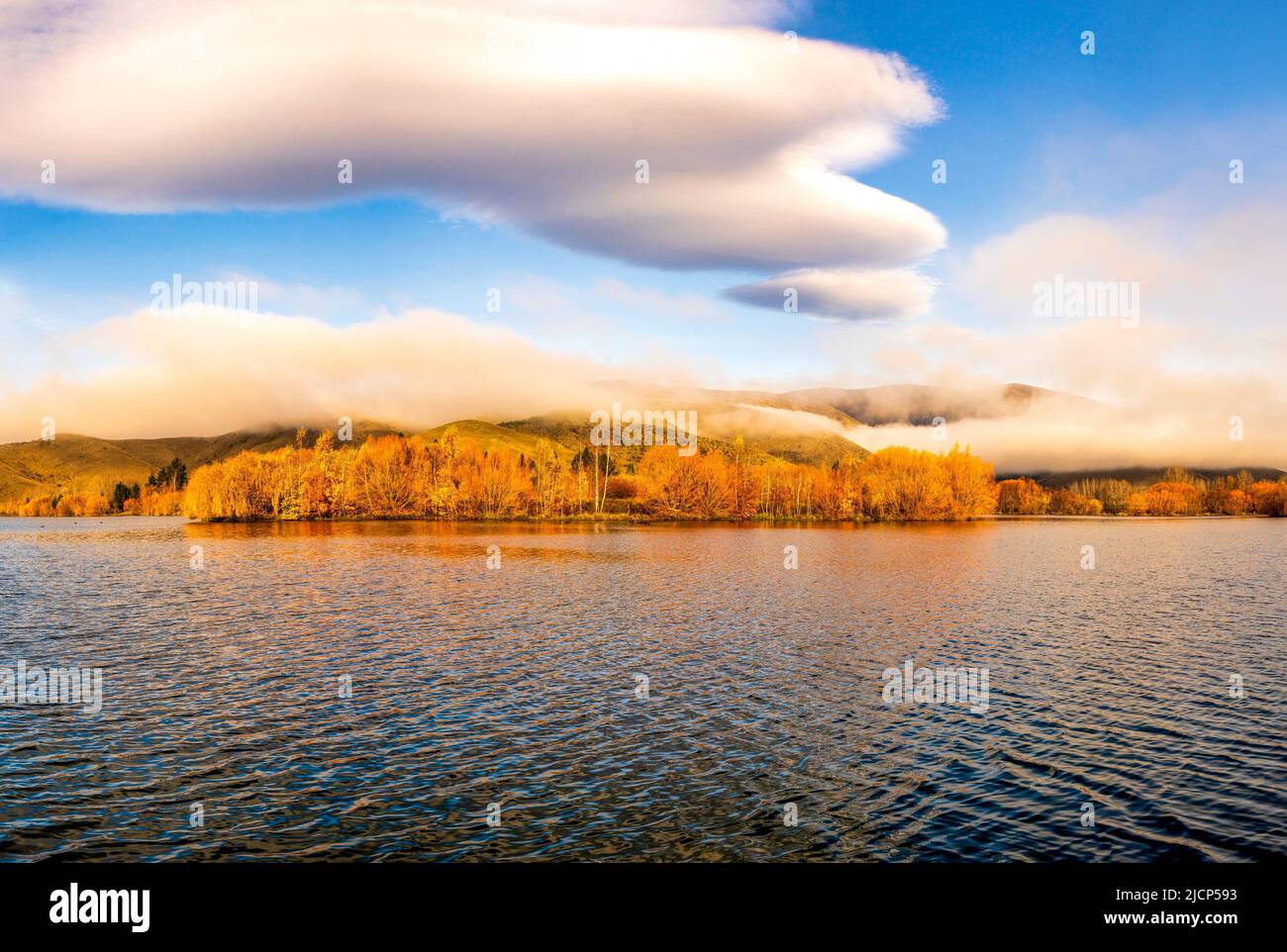 Wispy cumulus  cloud hovering over the Lakeside autumnal tree colour Stock Photo
