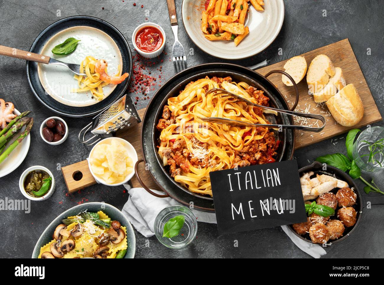 Table of italian meals on plates pasta Bolognese, ravioli, penne with chicken, sauces, parmesan and water on dark background. Top view. Stock Photo