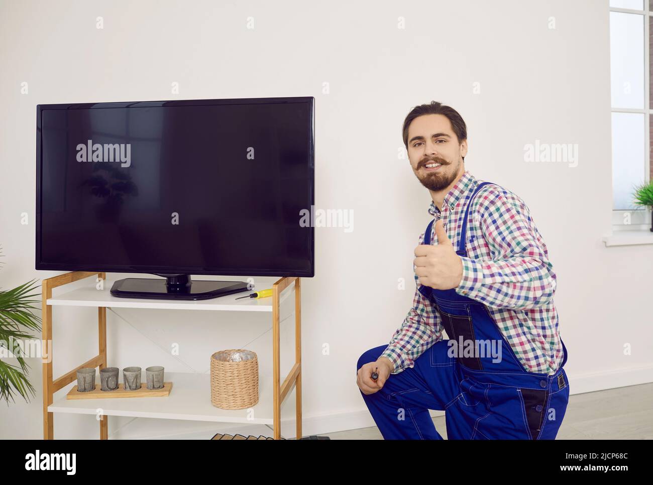 Happy technician showing thumbs up after he has repaired or installed television set Stock Photo