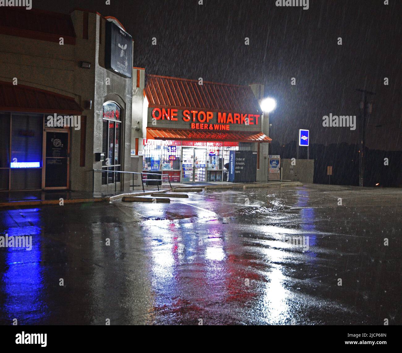 Lights reflected on the wet parking lot of the One Stop Market Beer and Wine store on a rainy night in Irving, Texas Stock Photo