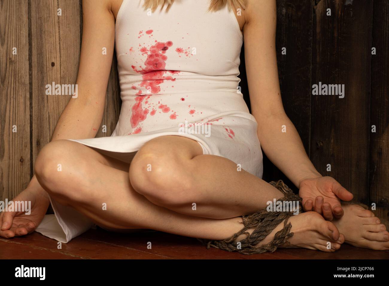 Ukrainian girl in a white dress with blood stains on the dress, tortured by Russian soldiers in the corner of the room, war in Ukraine, protest action Stock Photo