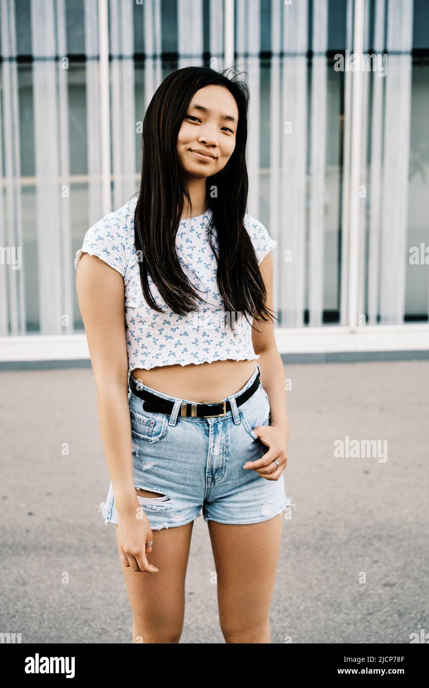 Young Asian woman looking at camera and smiles while standing outdoors. Stock Photo