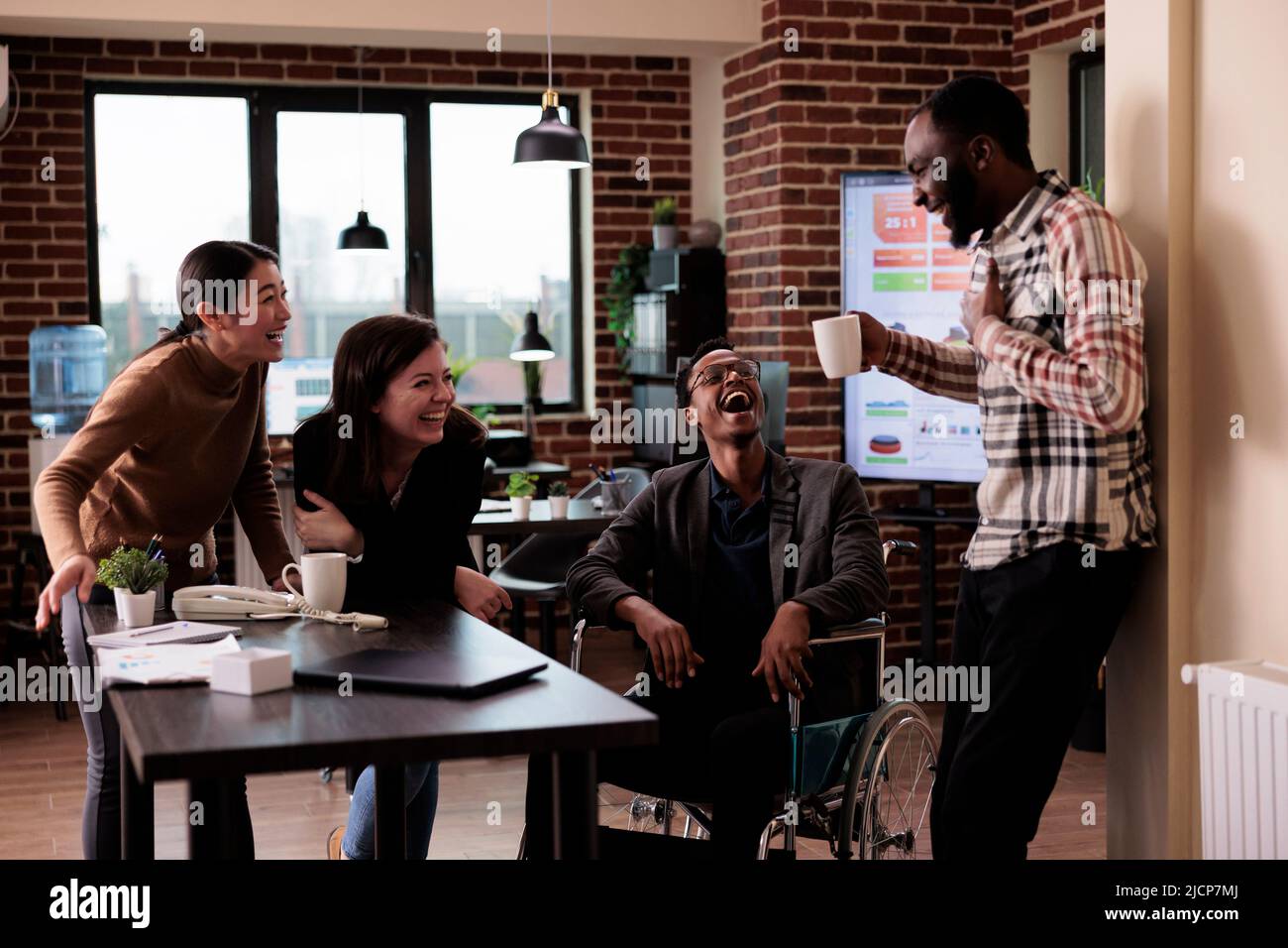 Diverse team of smiling workers and paralyzed man taking break from ...