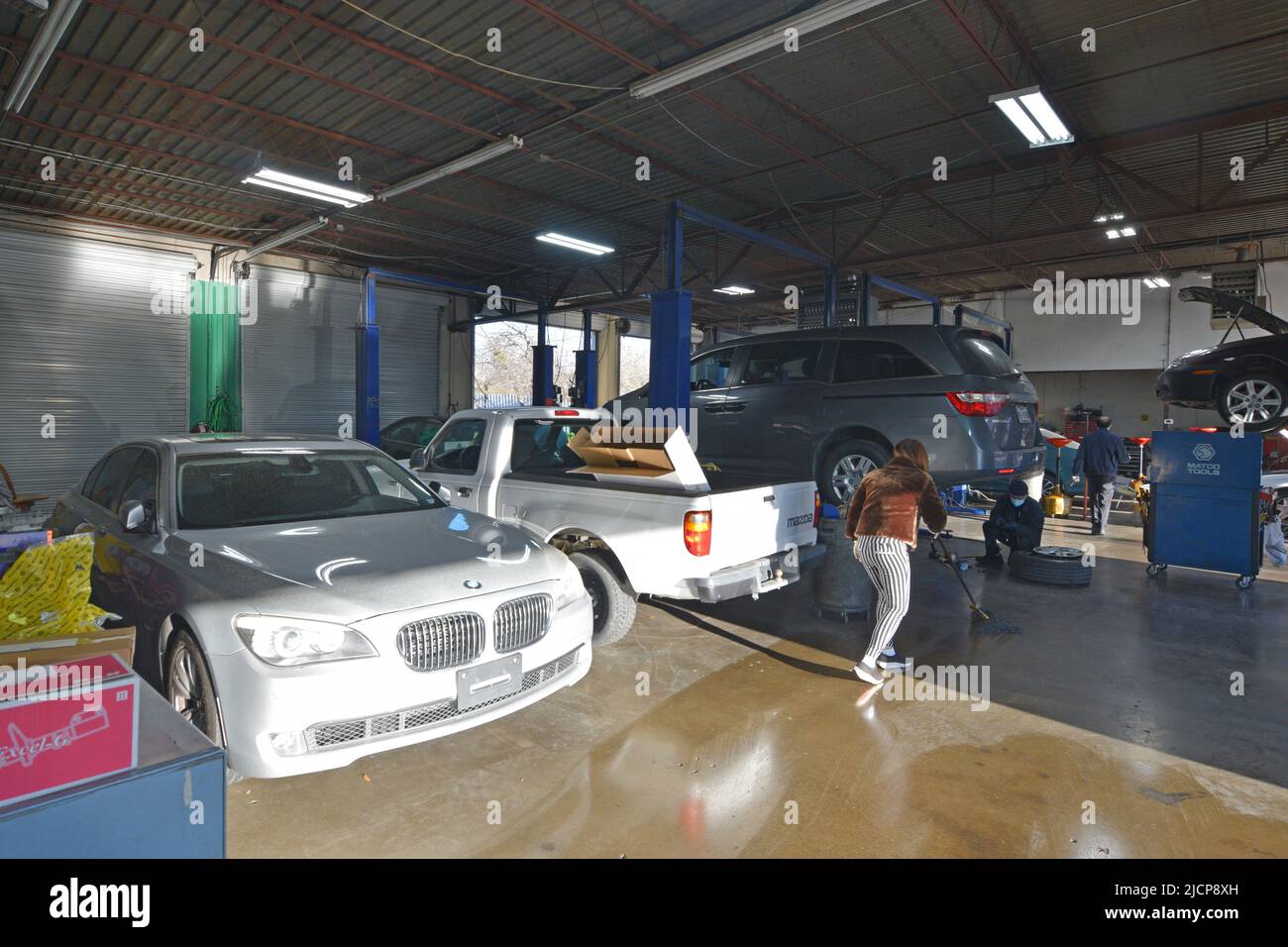 Woman mopping floor in an area of a car repair shop, cars on a rack or hydraulic lift in the background Stock Photo