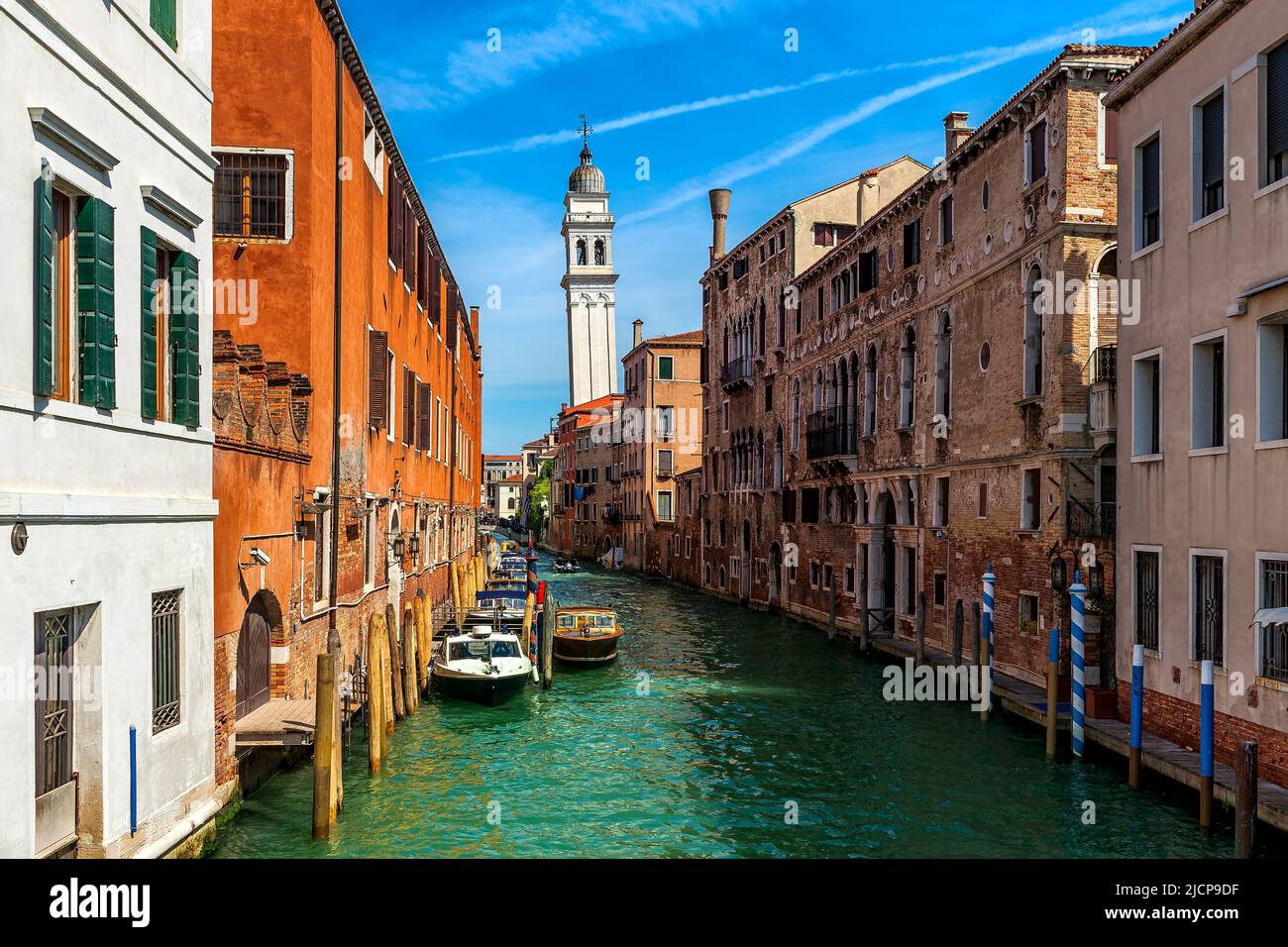 View of boats on narrow canal among old houses as leaning bell tower on background in Venice, Italy. Stock Photo