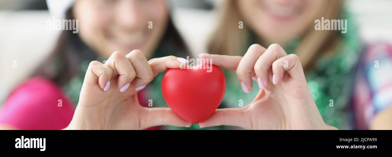 Sisters holding plastic red heart in hands and smiling Stock Photo