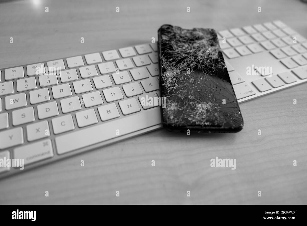 a completely destroyed cell phone lies on a computer keyboard Stock Photo