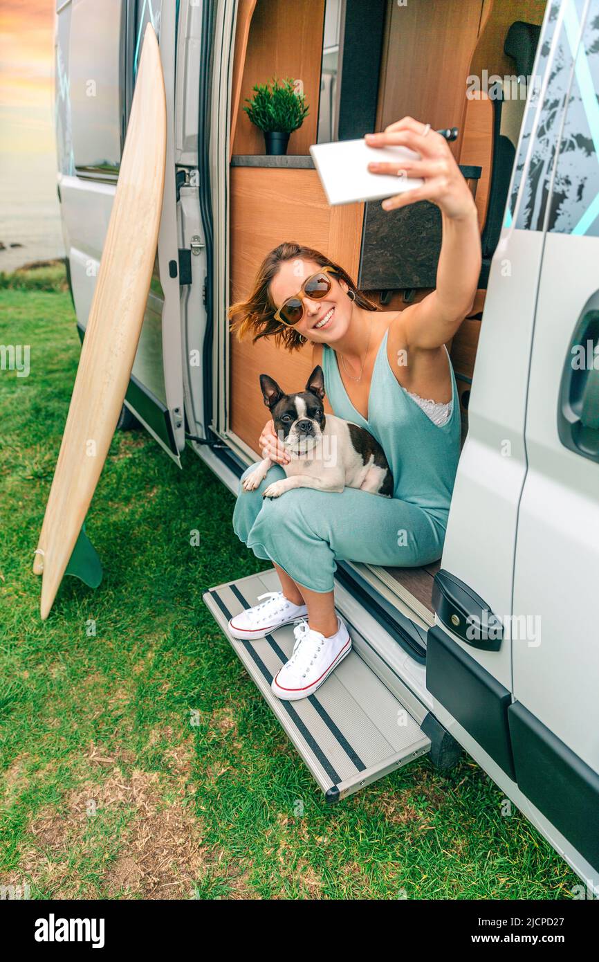 Woman taking photo sitting with her dog at door of camper van Stock Photo
