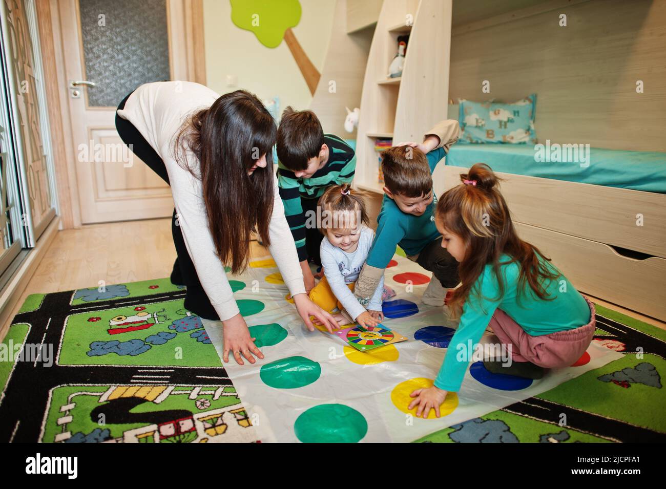 Happy family having fun together,four kids and mother playing twister game at home. Stock Photo