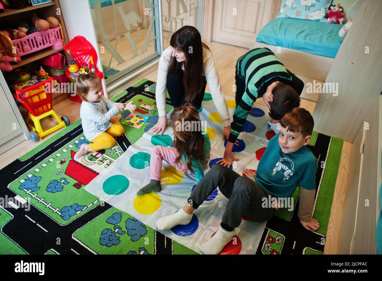 Happy family having fun together,four kids and mother playing twister game at home. Stock Photo