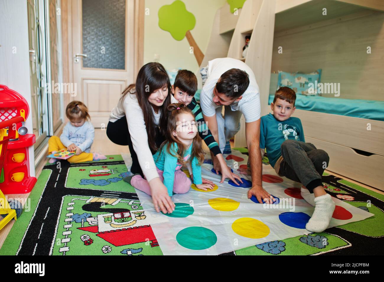Happy big family having fun together,four kids playing twister game at home. Stock Photo