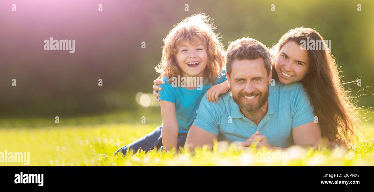 Family of mother dad and son child relax in summer park. Banner of Happy family Lying on grass. Young mother and father with child son play in the Stock Photo