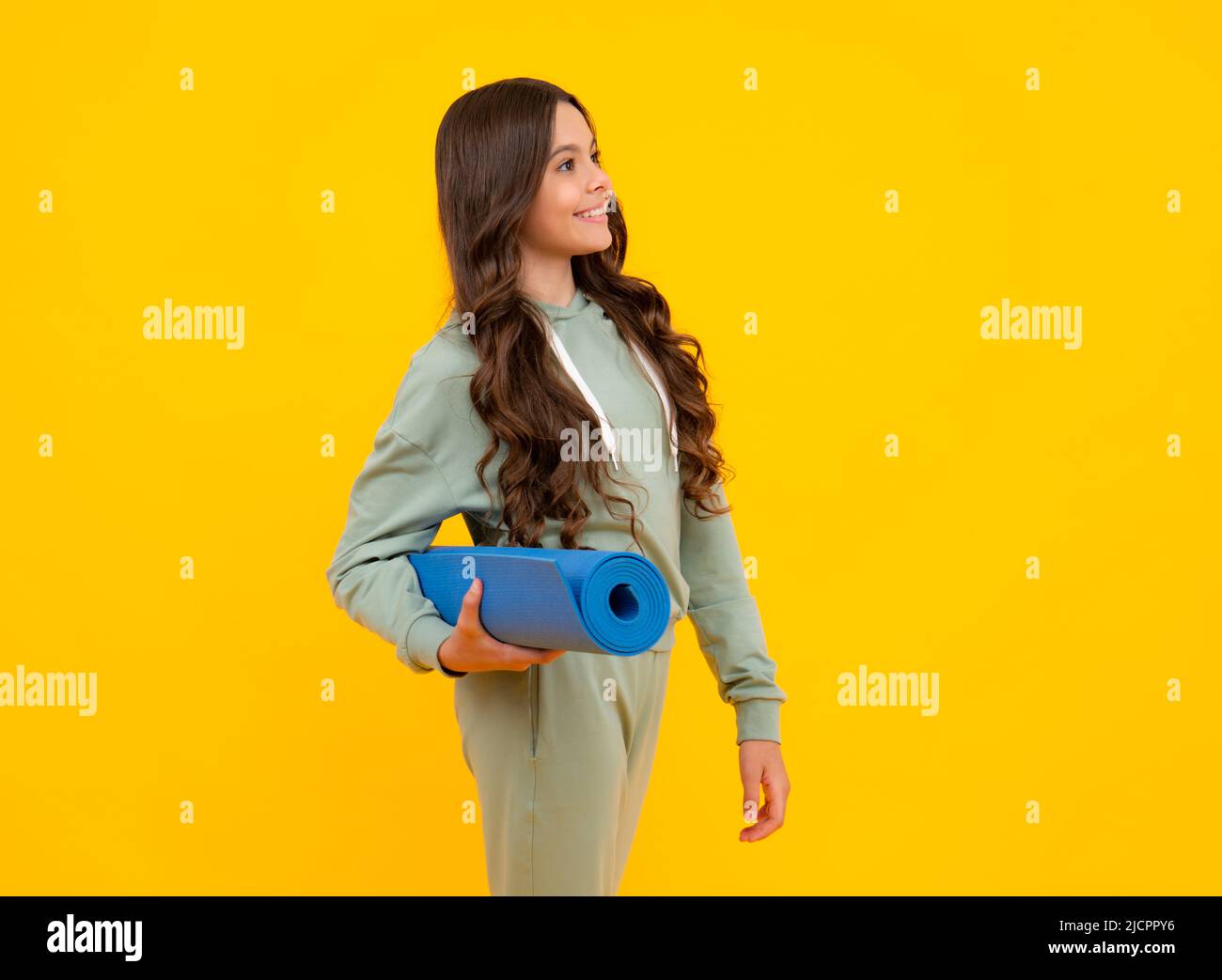 Sportswear advertising concept. Teenager child girl in tracksuits jogging suit posing in the studio hold fitness mat. Stock Photo