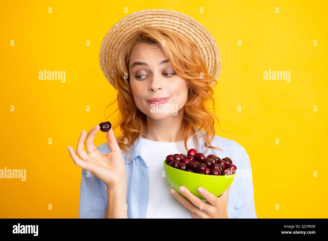 Young woman eats sweet cherries. Portrait of a beautiful girl with cherry on yellow background. Summer fruit picking season. Natural vitamins. Stock Photo