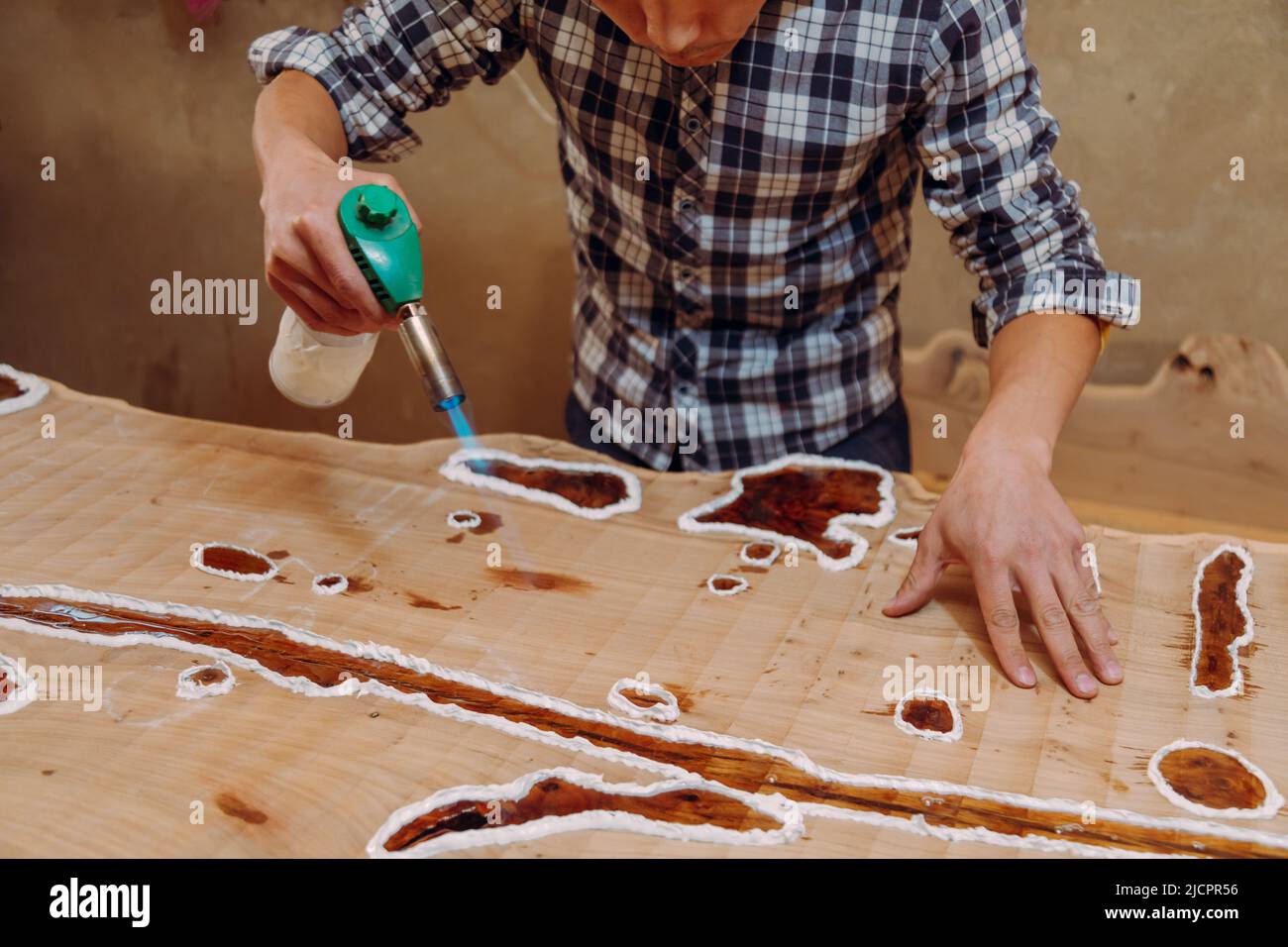 Carpenter removing air bubbles with blowtorch from epoxy table. Process