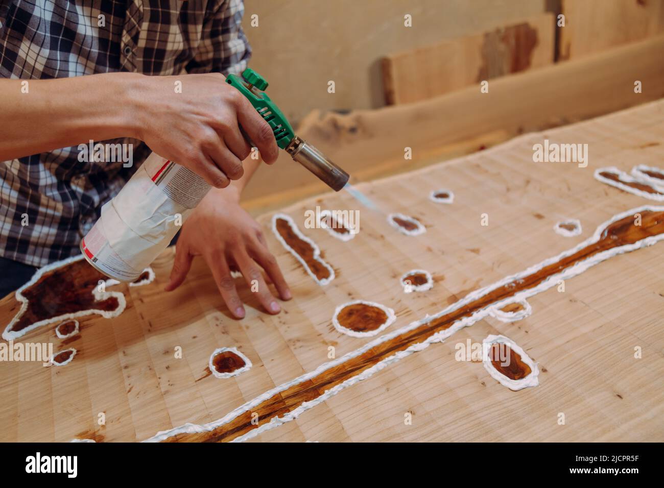 Carpenter removing air bubbles with blowtorch from epoxy table. Process