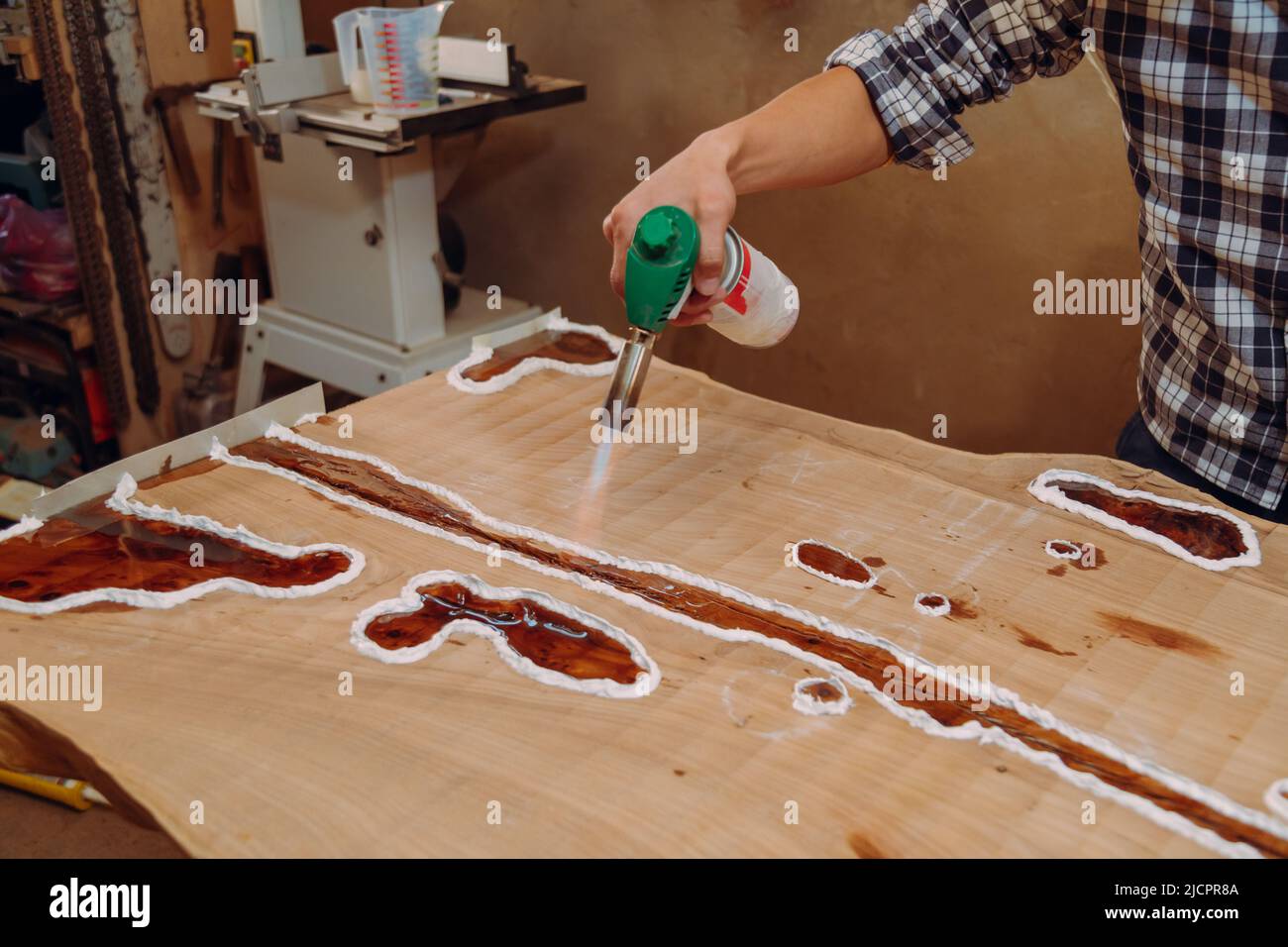 Carpenter removing air bubbles with blowtorch from epoxy table. Process
