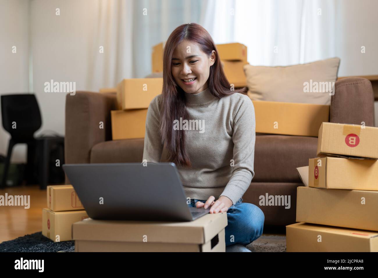 Asian woman entrepreneur using laptop for checking order, online market packing box delivery,Startup successful small business owner,SME, concept Stock Photo