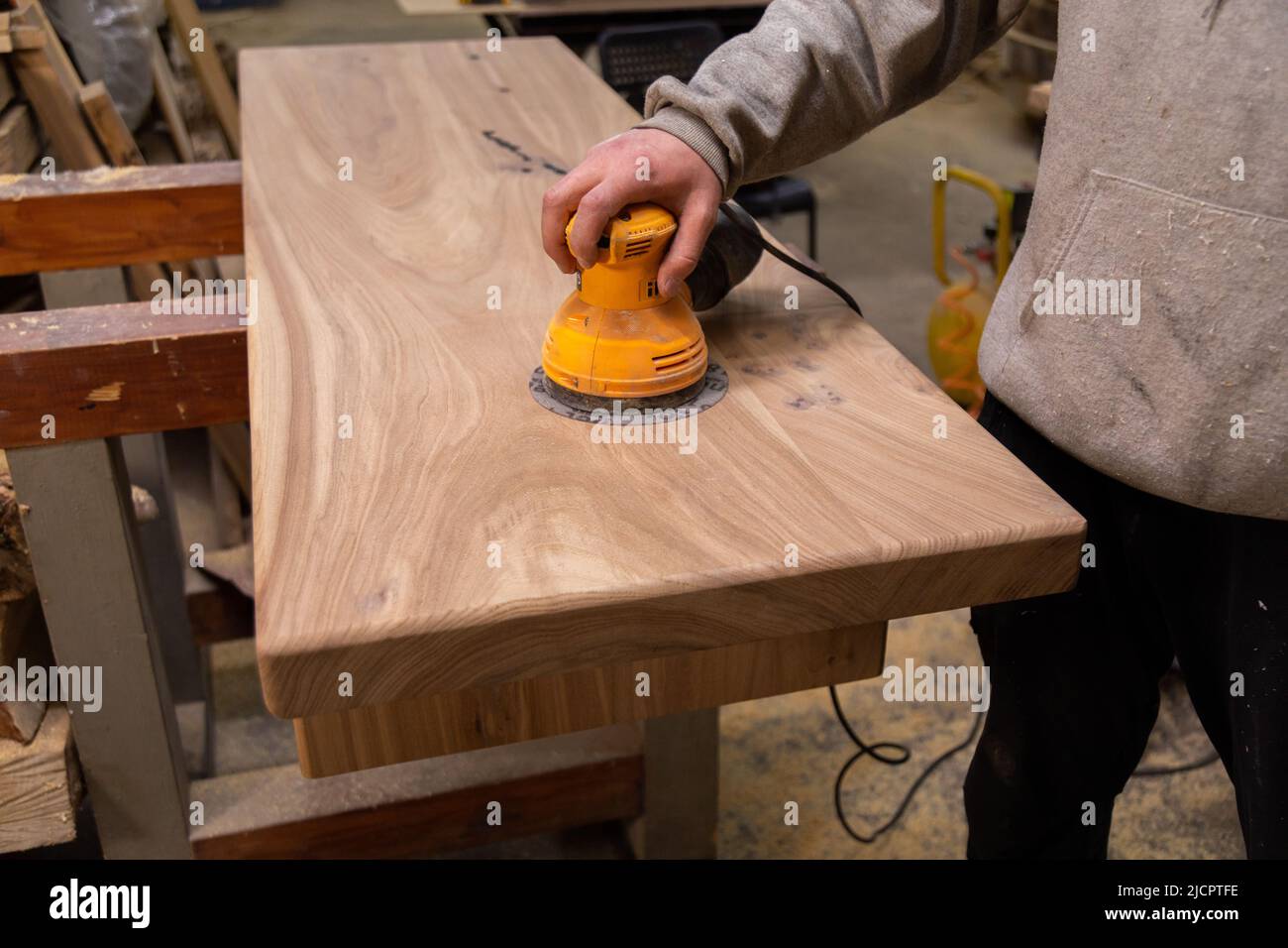 Closeup of carpenter sanding wood table with orbital sander in a