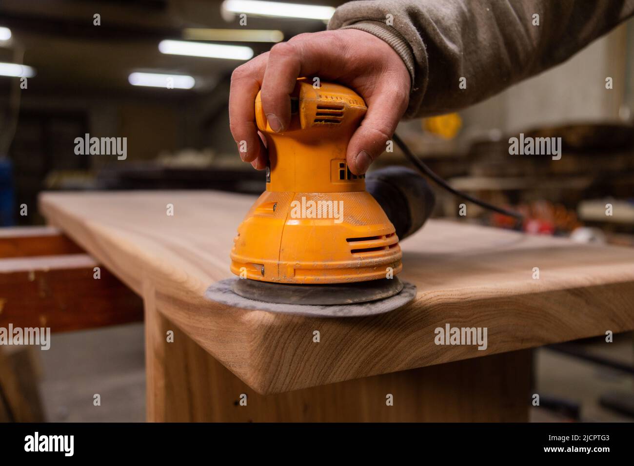 Closeup of carpenter sanding wood table with orbital sander in a
