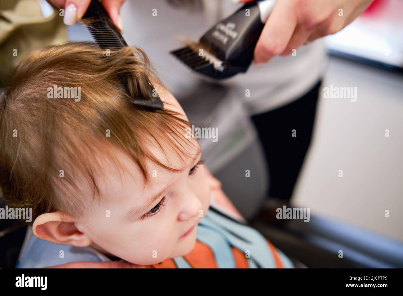 The hairdresser cuts the toddler baby boy in the Child first haircut. Kid age one