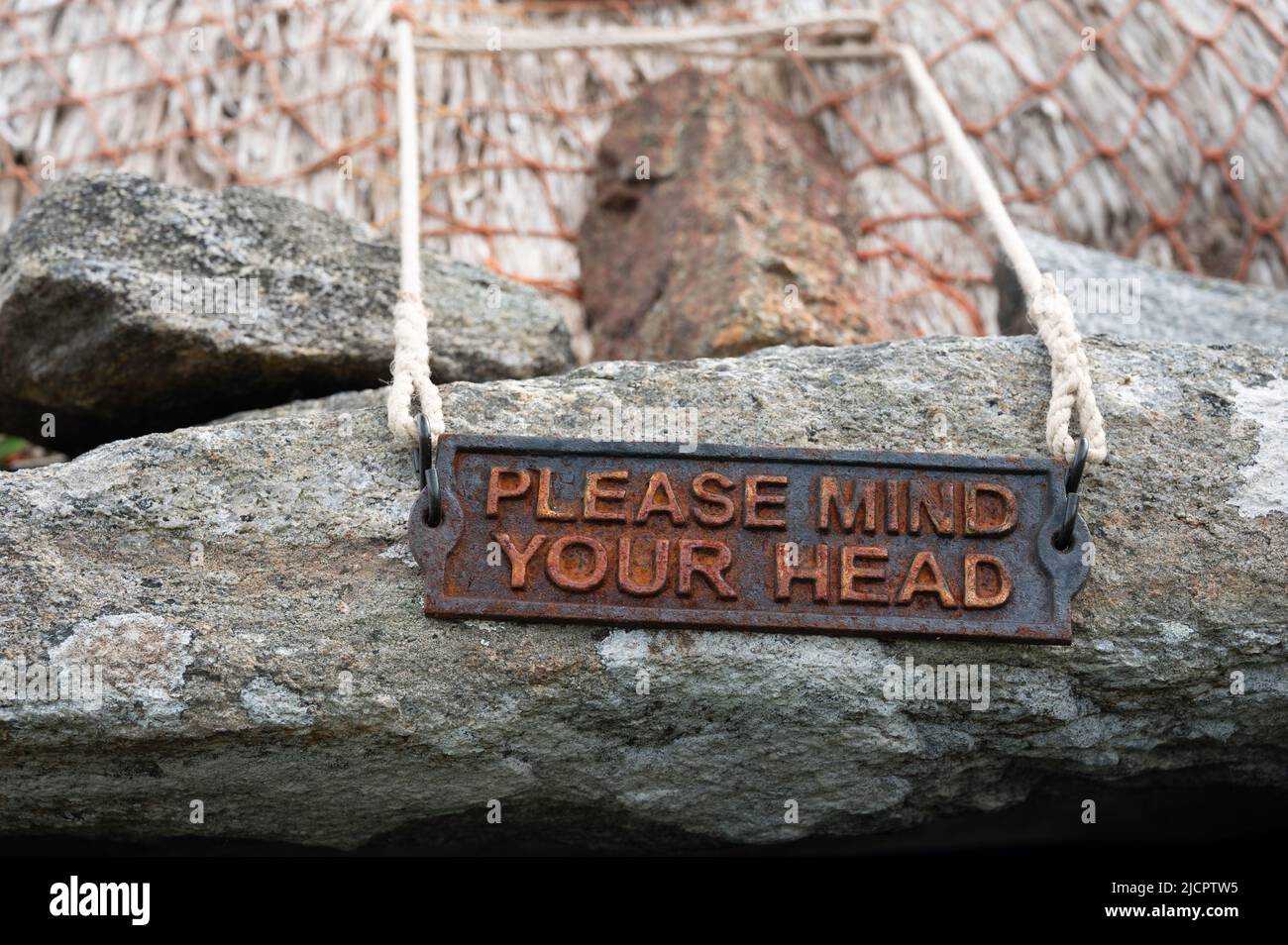 Rustic metal please mind your head sign on stone with blurred background of thatched roof. Norse mill, Shawbost, Isle of Lewis, Scotland, UK. Stock Photo